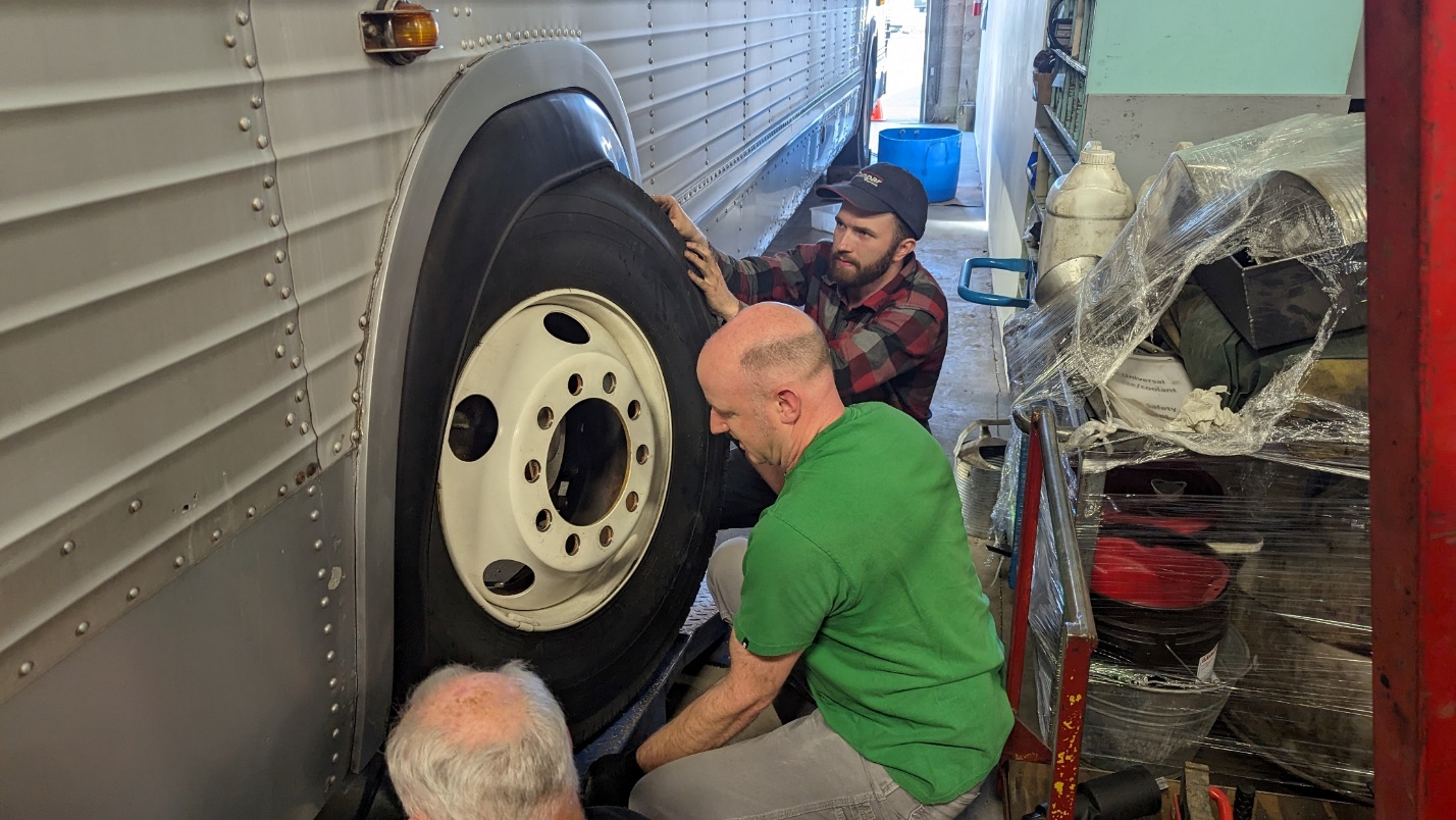 A group of men looking at a tire

Description automatically generated